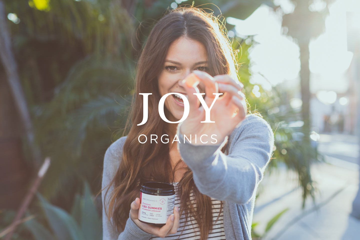 Joy Organics lifestyle photograph with a woman holding a gummy and the white Joy Organics wordmark